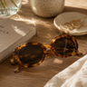 Tortoiseshell sunglasses on a wooden surface with a book and decorative items.