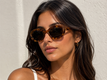 Woman wearing tortoiseshell sunglasses against a light background