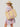 Woman in a colorful dress and straw hat holding a large straw bag with pink straps on a light gray background