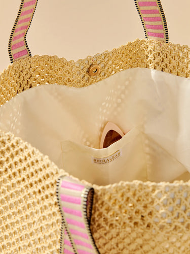 Close-up of a beige woven bag with pink and black striped handles and a visible brand label.