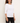 A woman modeling a white three-quarter sleeve crewneck top, paired with black pants, against a plain off-white background.