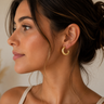 Close-up of a woman wearing gold hoop earrings with a neutral background