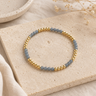 a light blue and gold beaded bracelet on a neutral background