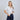 Woman wearing a white shirt and navy pants against a plain background