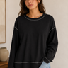 Woman wearing a black sweater with white trim in a neutral setting