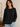 Woman wearing a black sweater with white trim in a neutral setting