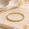 a 4mm gold beaded bracelet on a neutral background 