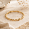 A gold beaded bracelet on a neutral background 
