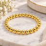 A gold beaded stretch bracelet made of polished metallic spherical beads, displayed on marbled table.