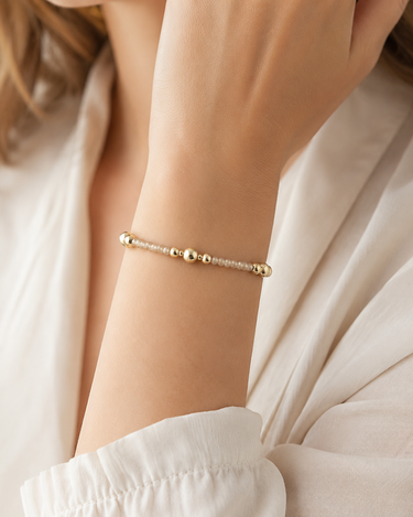 A woman wearing a gold and champagne shimmer beaded bracelet