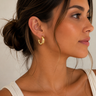 Woman wearing gold hoop earrings and a necklace against a neutral background