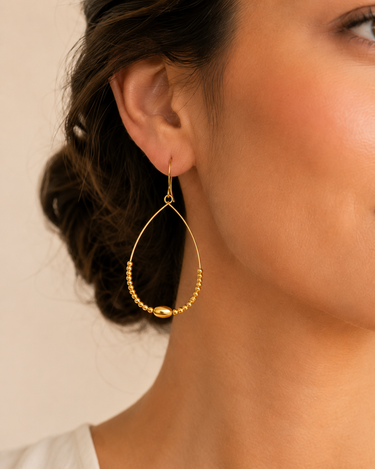 A woman wearing Gold beaded teardrop earrings