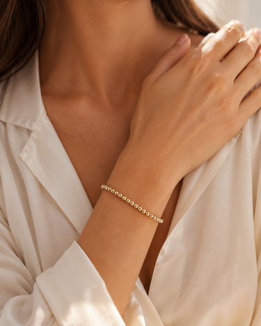 a woman wearing a 4mm gold beaded bracelet on a neutral background 