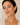A close-up of a woman wearing gold teardrop hoop earrings with a small clear stone accent, set against a soft beige background.