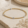 a oval silver and circle gold beaded bracelet on a neutral background