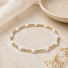a gold and white beaded bracelet on a neutral background