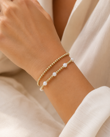 a woman wearing a gold and white beaded bracelet stacked with a gold beaded bracelet