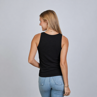 Woman wearing a black tank top and blue jeans on a plain background