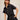 Woman wearing a black romper with gold buttons against a beige background