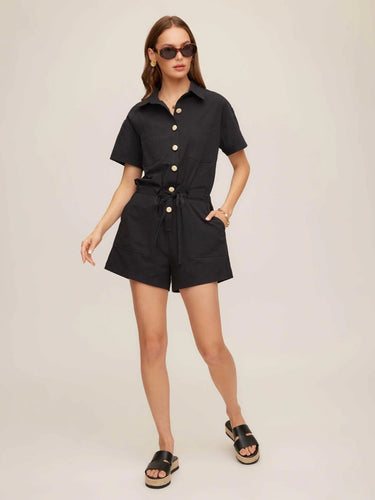 Woman wearing a black romper with buttons on a beige background