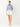 A woman modeling a blue and white vertically striped button-down shirt with rolled sleeves and white shorts, standing against a plain white studio background.