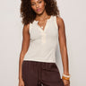 Woman wearing a white sleeveless top and brown pants on a plain background