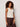 Woman wearing a white sleeveless top and brown pants against a plain background