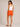 Woman wearing orange shorts and a white tank top on a beige background