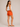 Woman wearing orange shorts and a white tank top on a beige background