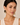 A close-up of a woman wearing gold geometric drop earrings with clear rectangular stones, set against a soft beige background.