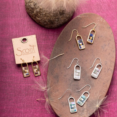 Set of earrings on a wooden stand with 'Scout' branding on a pink fabric background