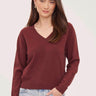 a woman wearing a deep wine red v-neck pullover sweater and blue jeans on a white background 
