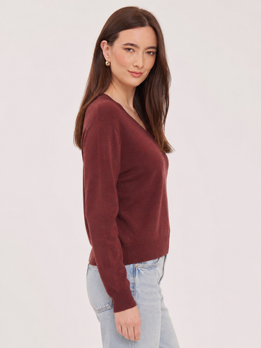a woman wearing a deep wine red v-neck pullover sweater and blue jeans on a white background 