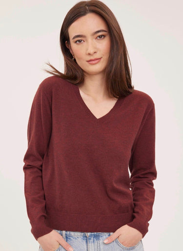 a woman wearing a deep wine red v-neck pullover sweater and blue jeans on a white background 