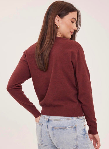 a woman wearing a deep wine red v-neck pullover sweater and blue jeans on a white background 