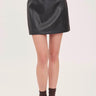A woman wearing a faux leather skirt in black with brown loafers on a white background.