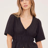 A woman wearing a v neck poplin top with ruching at the center on a white background