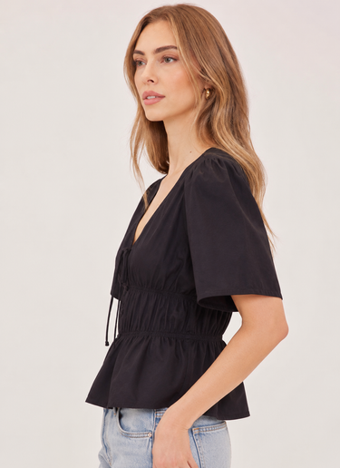 A woman wearing a v neck poplin top with ruching at the center on a white background