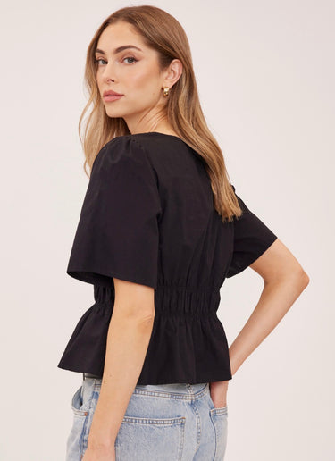 A woman wearing a v neck poplin top with ruching at the center on a white background