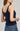 Woman wearing a navy blue knitted tank top and blue jeans on a light gray background