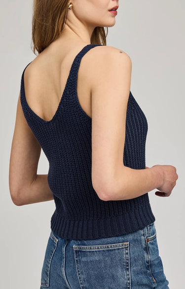 Woman wearing a navy blue knitted tank top and blue jeans on a light gray background