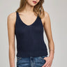 Woman wearing a navy blue knitted tank top and blue jeans on a gray background