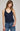 Woman wearing a navy blue knitted tank top and blue jeans on a gray background