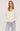 A woman wearing a cream v-neck pullover and blue jeans on a white background