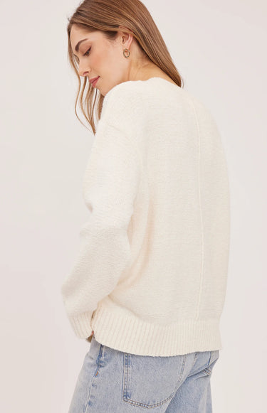 a woman turning to the side in a white pullover with blue jeans on a white background