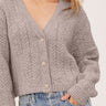 A woman wearing a knit heather V- neck cardigan and blue jeans on a white background