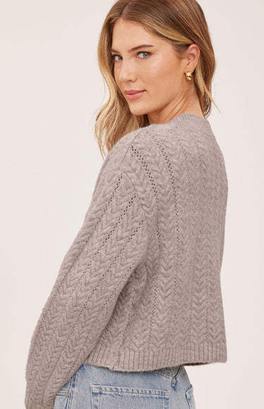 A woman wearing a knit heather cardigan and blue jeans on a white background