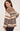 A woman wearing a brown, cream, and dark brown knit sweater with geometric patterns, shown from a three-quarters back view against a light beige studio background.