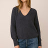 A woman  wearing a gray ribbed v-neck sweater and jeans on a white background