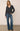 A woman  wearing a gray ribbed v-neck sweater and jeans on a white background